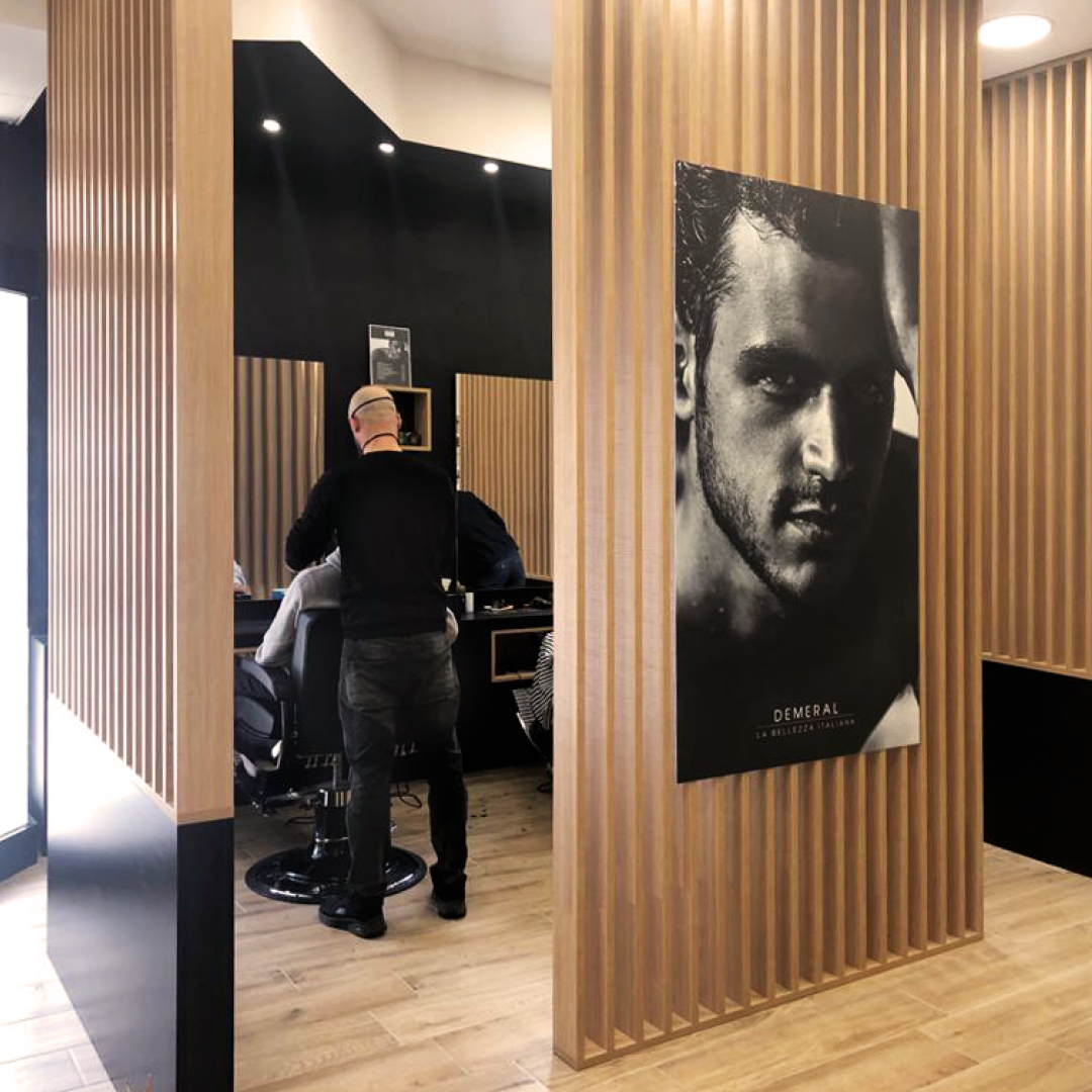 Immagine della zona barber di un salone in cui si vede il parrucchiere tagliare di spalle nella poltrona barber
